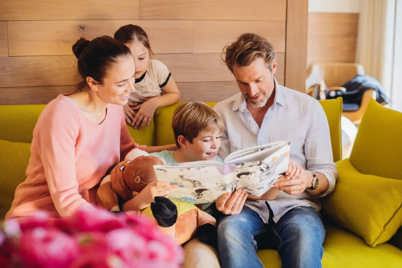 Familie liest gemeinsam ein Buch auf einem Sofa im Hotel Reiters Finest Family. Gemütliche Atmosphäre im Familienzimmer.