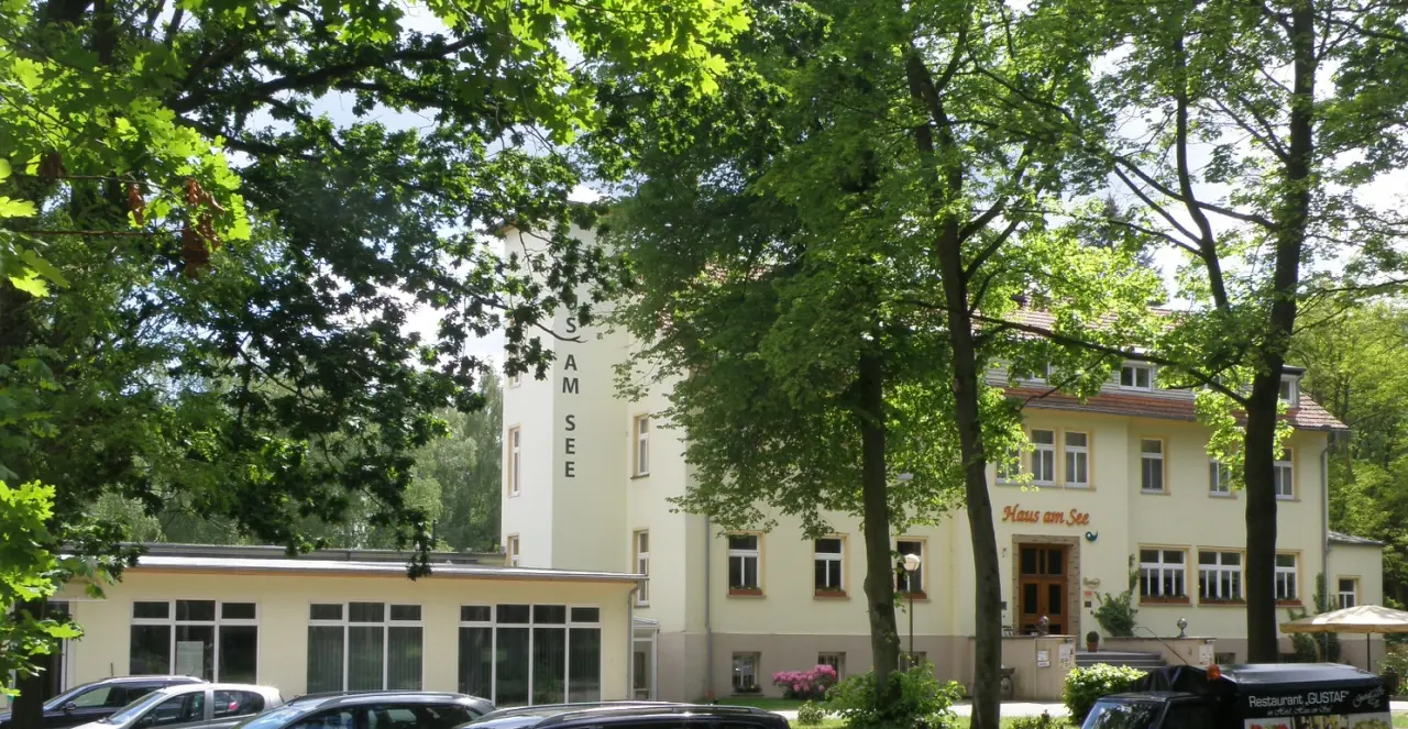 Aussenansicht des Wellness- & Sporthotels "Haus am See" umgeben von Bäumen an einem sonnigen Tag.