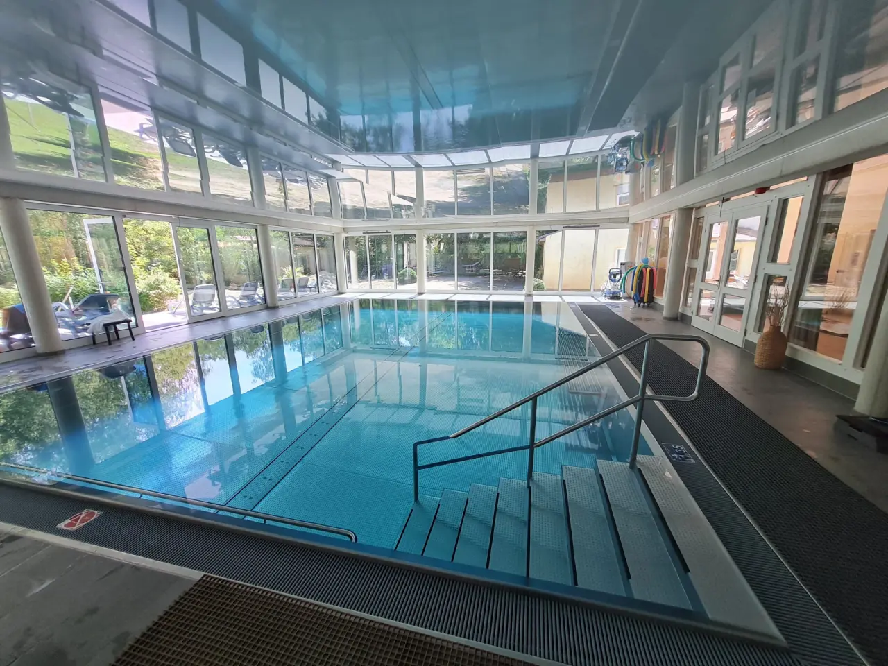 Heller Innenpool mit großen Panoramafenstern und Blick ins Grüne im Wellness-& Sporthotel 'Haus am See'.