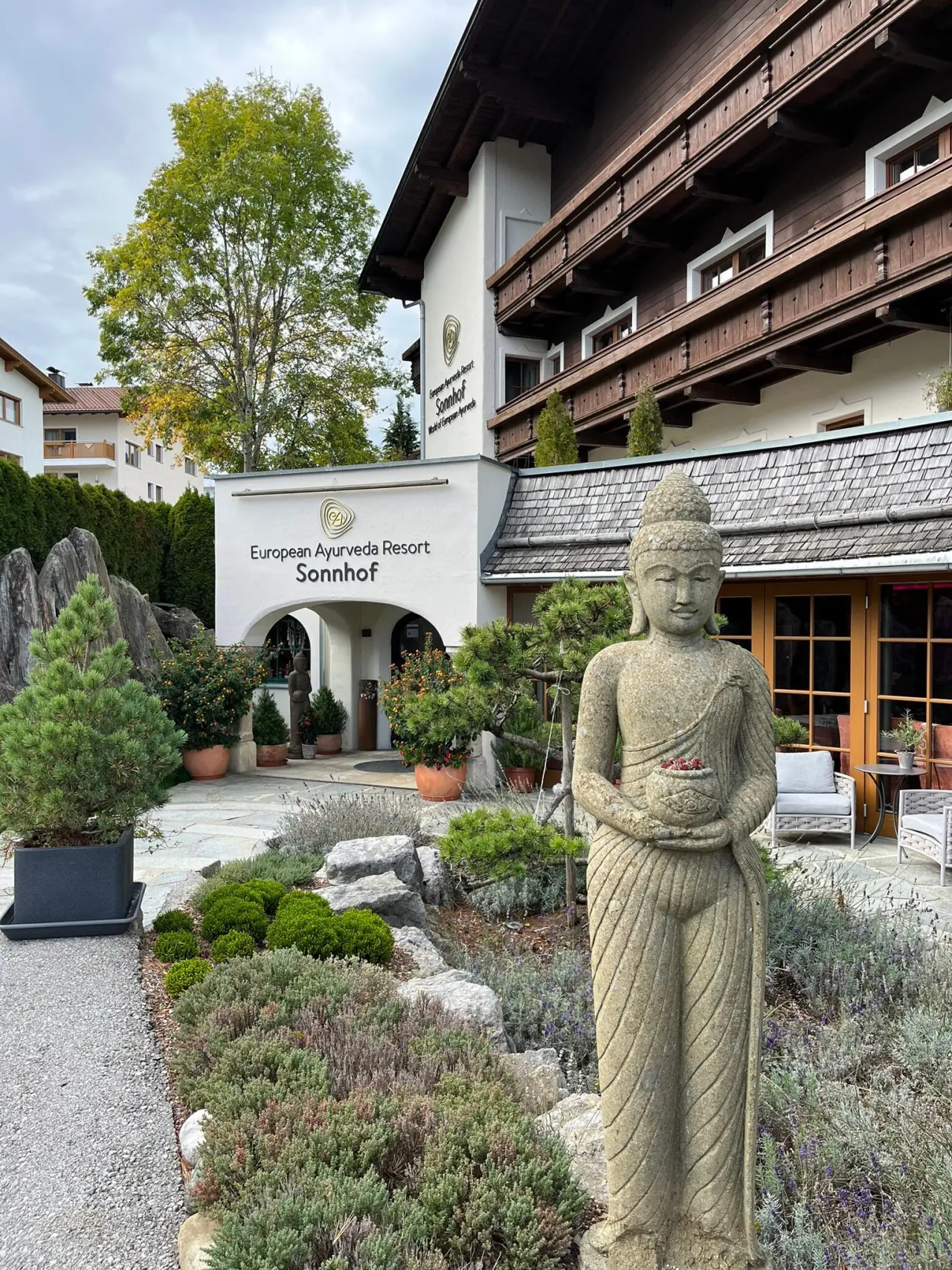 Aussenansicht des European Ayurveda Resort Sonnhof mit Buddha-Statue, einladendem Eingang und gepflegtem Garten.
