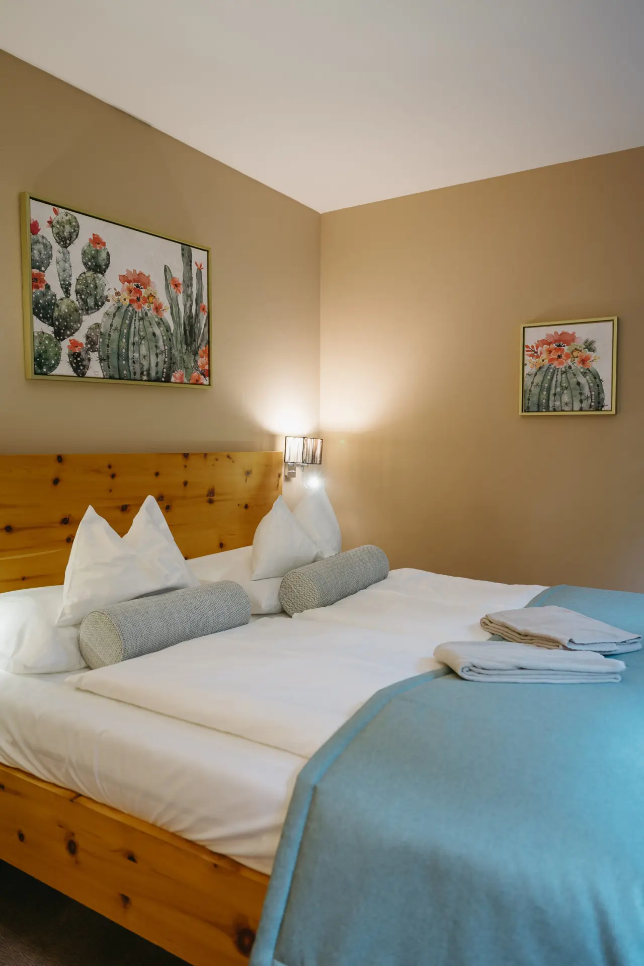 Gemütliches Doppelzimmer im Hotel Schlafgut mit Holzbett, weißen Kissen und Kakteenbildern an der Wand.