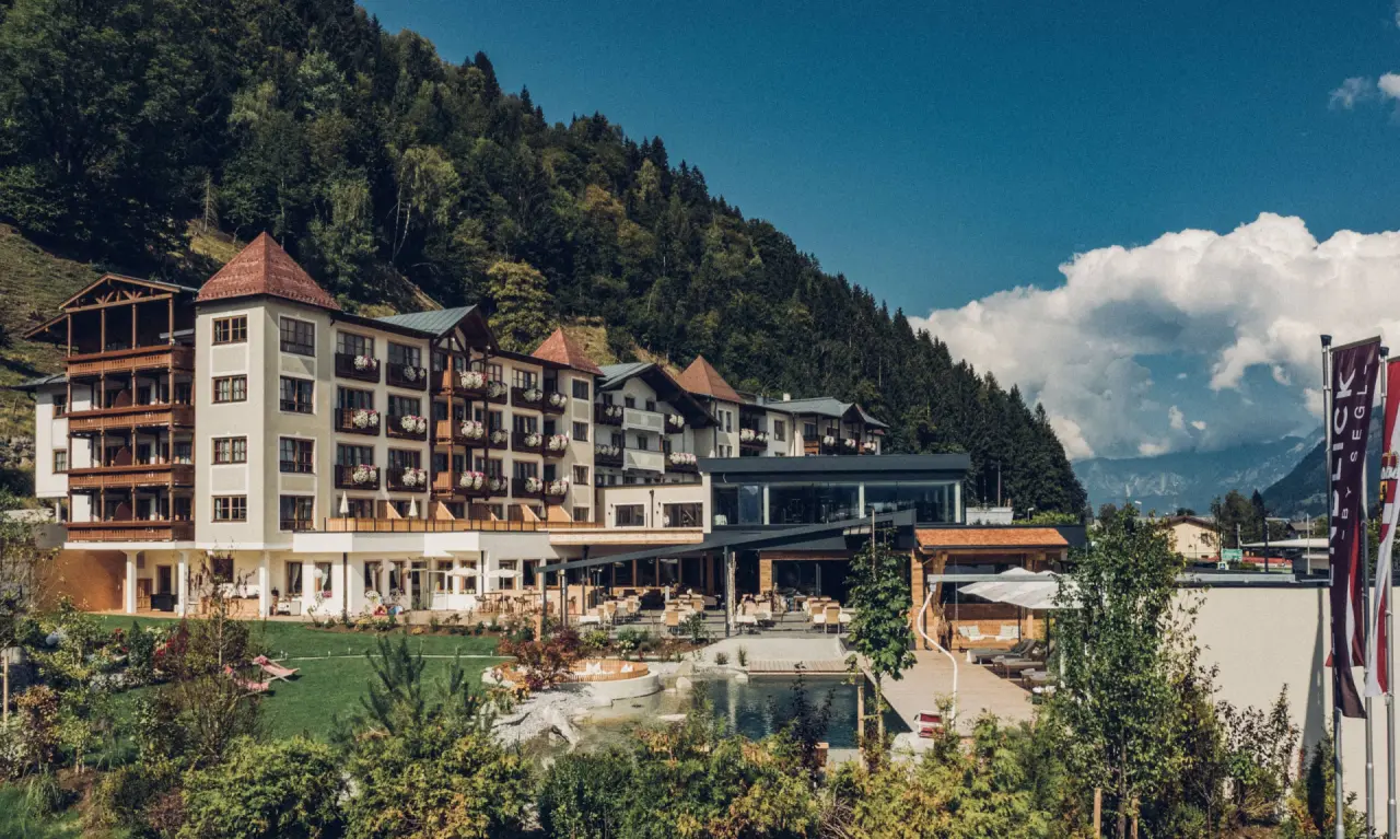 Panoramablick auf das Sportresort Alpenblick mit alpiner Architektur, Aussenpool, Sonnenterrasse und umliegenden Bergen.