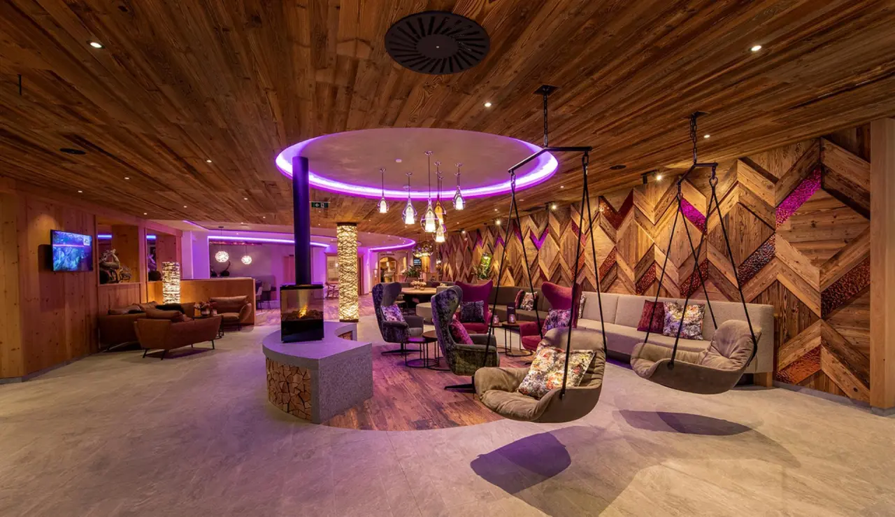 Moderne Hotellobby im Sportresort Alpenblick mit gemütlichen Sitzbereichen, Kamin und stilvoller Beleuchtung.