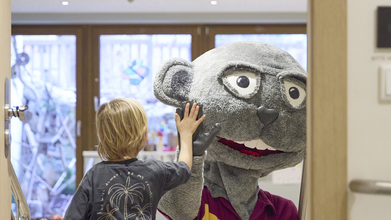 Das Bayrischzell Familotel Oberbayern in Bayrischzell – Kind begrüßt das Hotelmaskottchen im Innenbereich | Wellnesshotel Oberbayern