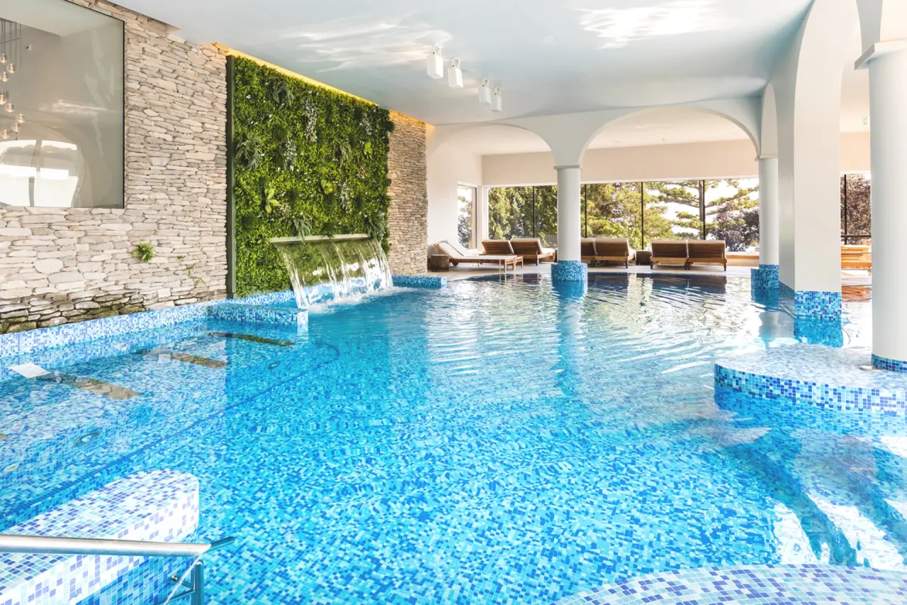 Grosszügiger Innenpool mit Wasserfall, grüner Wand und Blick ins Grüne im Wellnessbereich des Kurhaus Cademario.