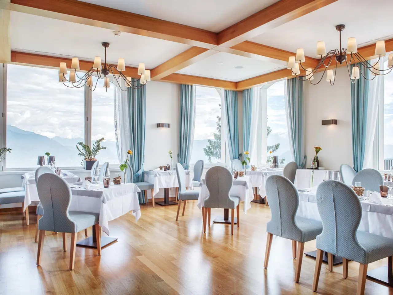 Helles Restaurant im Kurhaus Cademario mit elegant gedeckten Tischen und Panoramablick auf die Berge und den See.