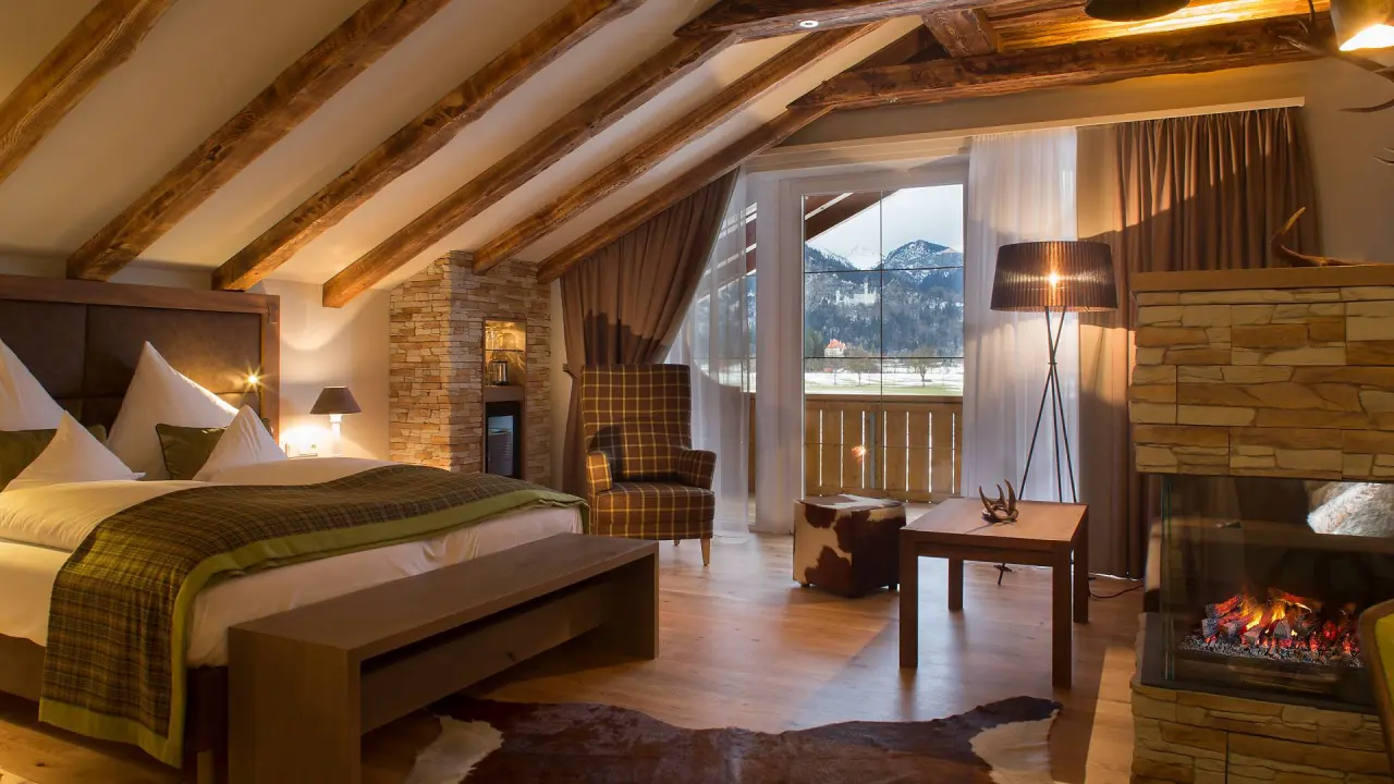 Luxuriöses Hotelzimmer im Das Rübezahl mit Kamin, Holzbalken und Bergblick auf Schloss Neuschwanstein.