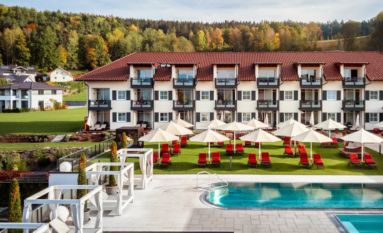 Außenansicht des Landromantik Wellness Hotel Oswald mit großem Außenpool, Liegewiese und herbstlichem Waldpanorama.