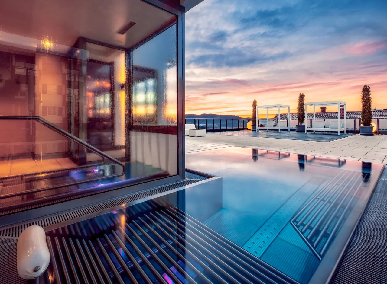 Dramatischer Sonnenuntergang über dem Rooftop-Pool des Landromantik Wellness Hotel Oswald mit Bergblick und Lounge-Betten.