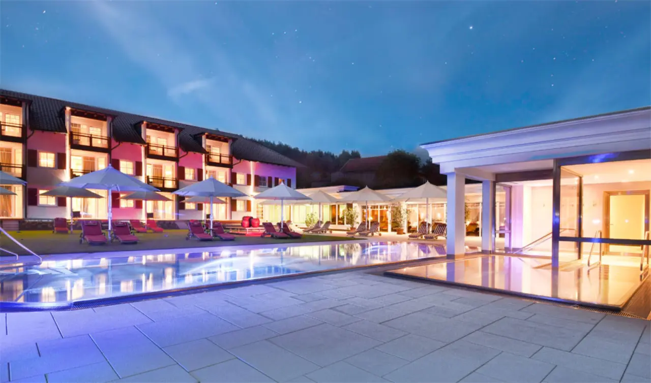 Beleuchteter Aussenpool und Hotelanlage des Landromantik Wellness Hotel Oswald bei Nacht unter sternenklarem Himmel.