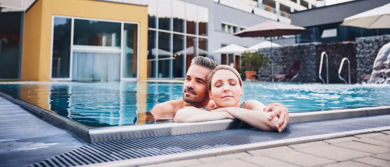 Entspanntes Paar im Aussenpool des Hotel Lebensquell mit moderner Architektur im Hintergrund.
