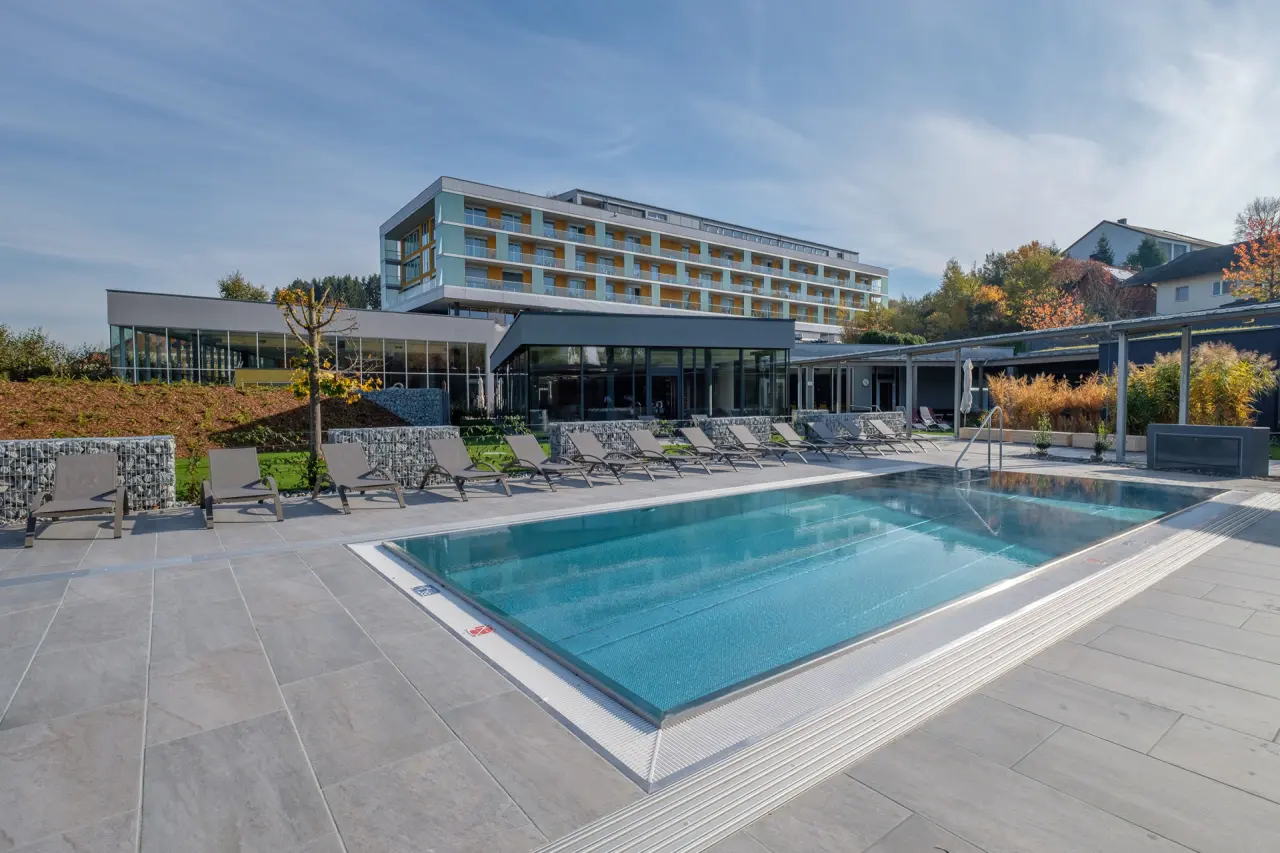 Moderner Aussenpoolbereich mit Liegen und dem Hotel Lebensquell im Hintergrund an einem sonnigen Herbsttag.