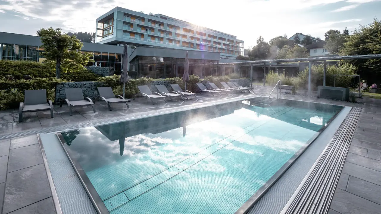 Beheizter Aussenpool mit Dampf und Liegen im Hotel Lebensquell. Moderne Architektur und grüne Umgebung bei Sonnenlicht.