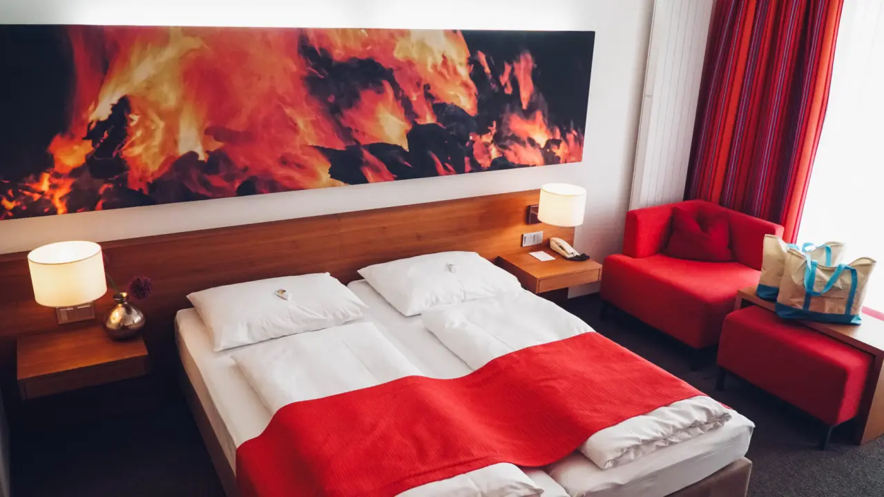 Modernes Doppelzimmer im Hotel Lebensquell mit roter Bettdecke, Sitzbereich und Kunstwerk über dem Bett.