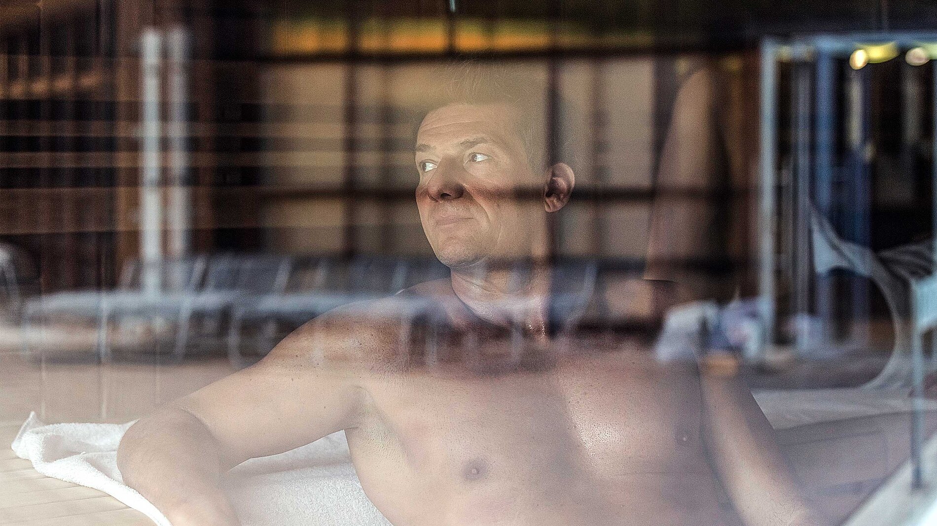 Dorint An den Thermen in Freiburg-Süd – Mann entspannt in der Sauna, durch Glas gesehen | Wellnesshotel Schwarzwald