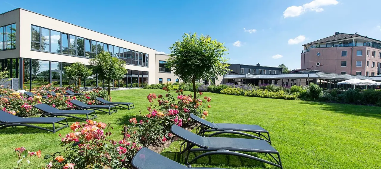 Gepflegter Hotelgarten mit Sonnenliegen und blühenden Rosen vor der modernen Architektur des See Park Janssen.