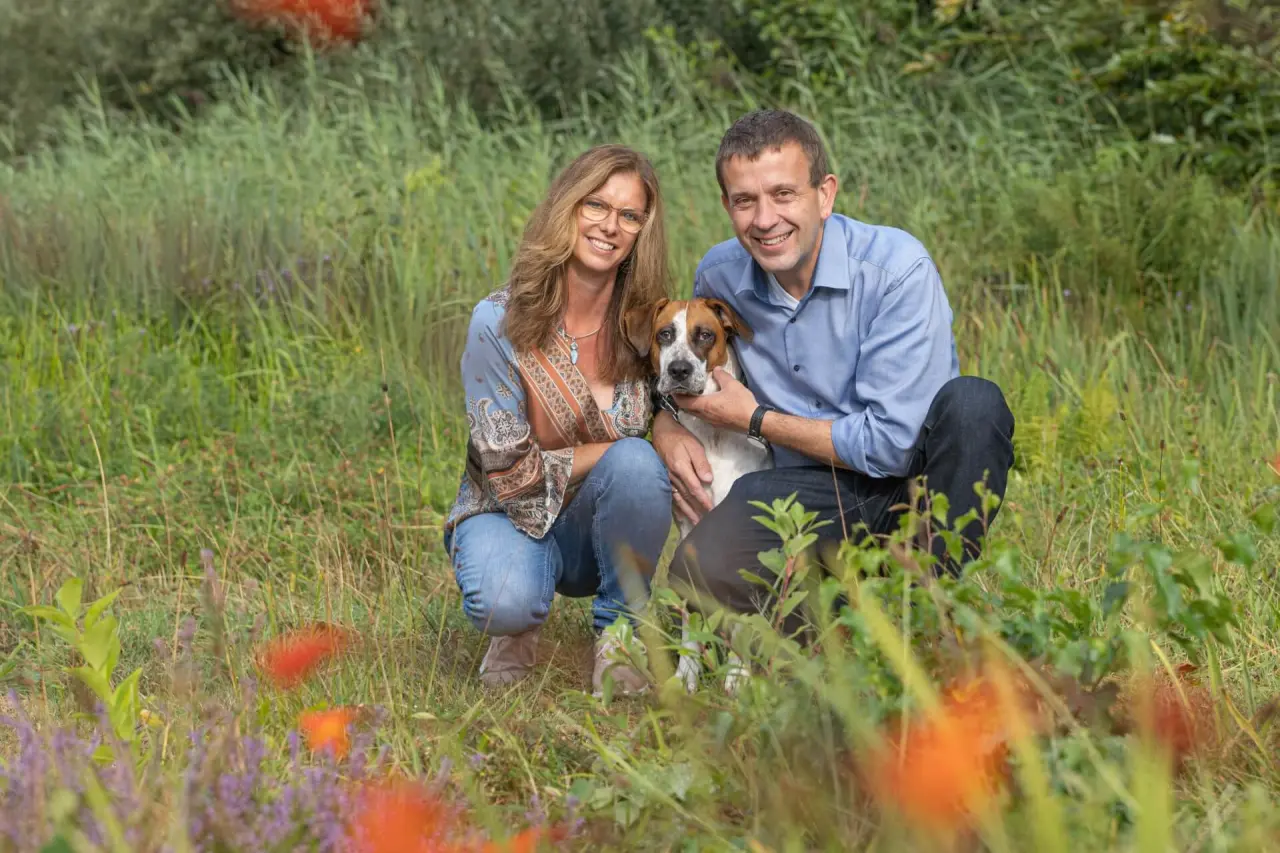 Laechelndes Paar mit Hund in einer natuerlichen Wiesenlandschaft. Ein Bild aus dem Umfeld des Ringhotel Köhlers Forsthaus.