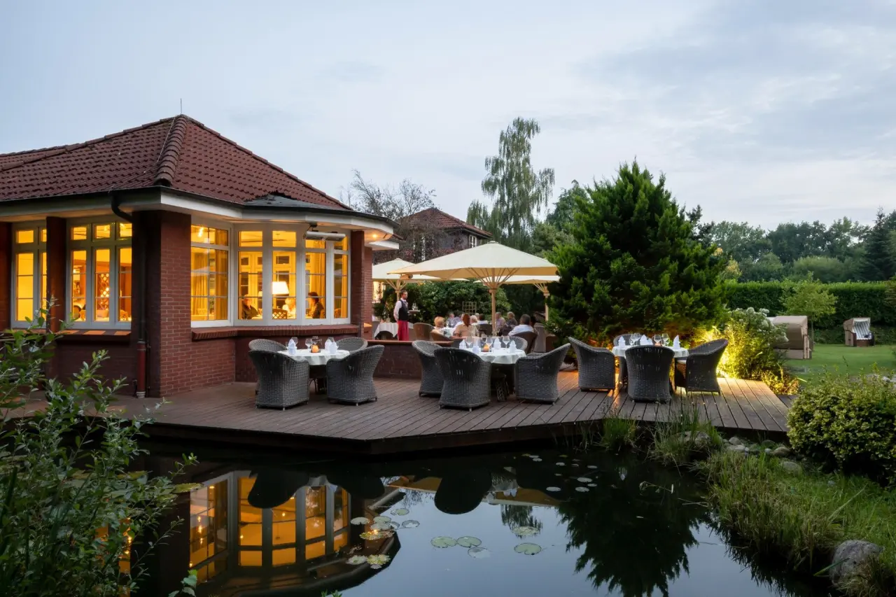 Abendstimmung auf der Restaurantterrasse am Teich des Ringhotel Köhlers Forsthaus mit beleuchteten Tischen und Gästen.
