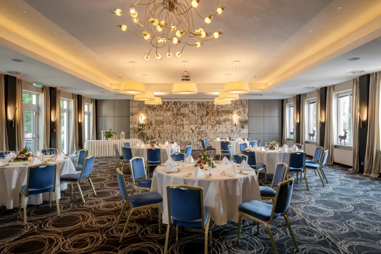 Festlich gedeckter Speisesaal im Ringhotel Köhlers Forsthaus mit blauen Stühlen, runden Tischen und eleganter Beleuchtung.