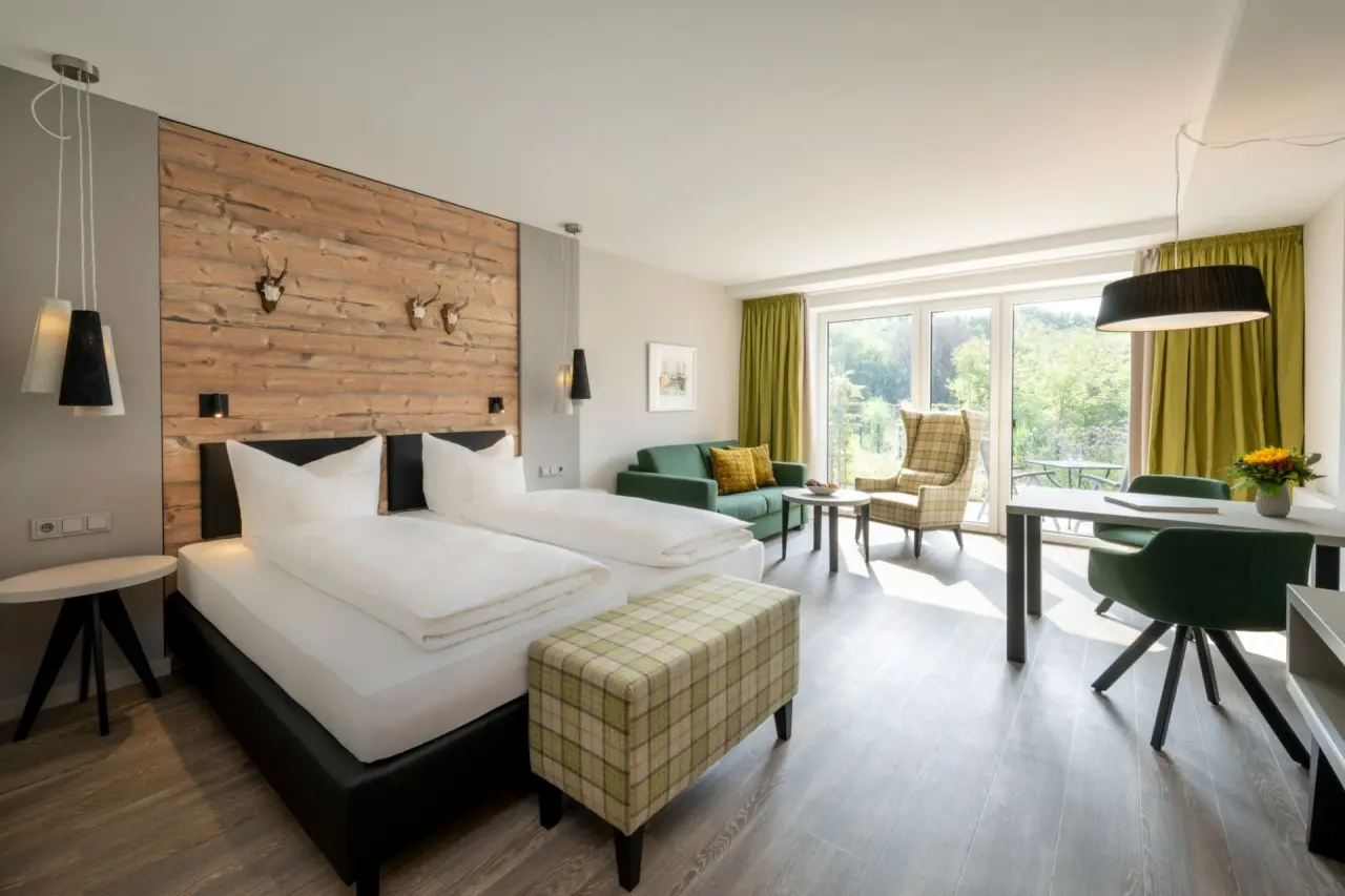 Geräumiges Hotelzimmer im Ringhotel Köhlers Forsthaus mit Doppelbett, Sitzbereich und Blick ins Grüne.