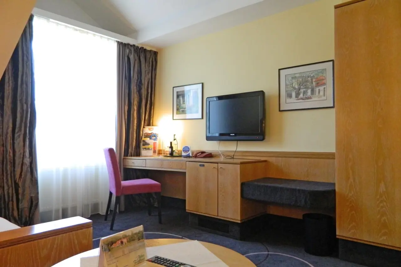 Helles Hotelzimmer mit Schreibtisch, pinkem Stuhl und Fernseher im Ringhotel Köhlers Forsthaus.