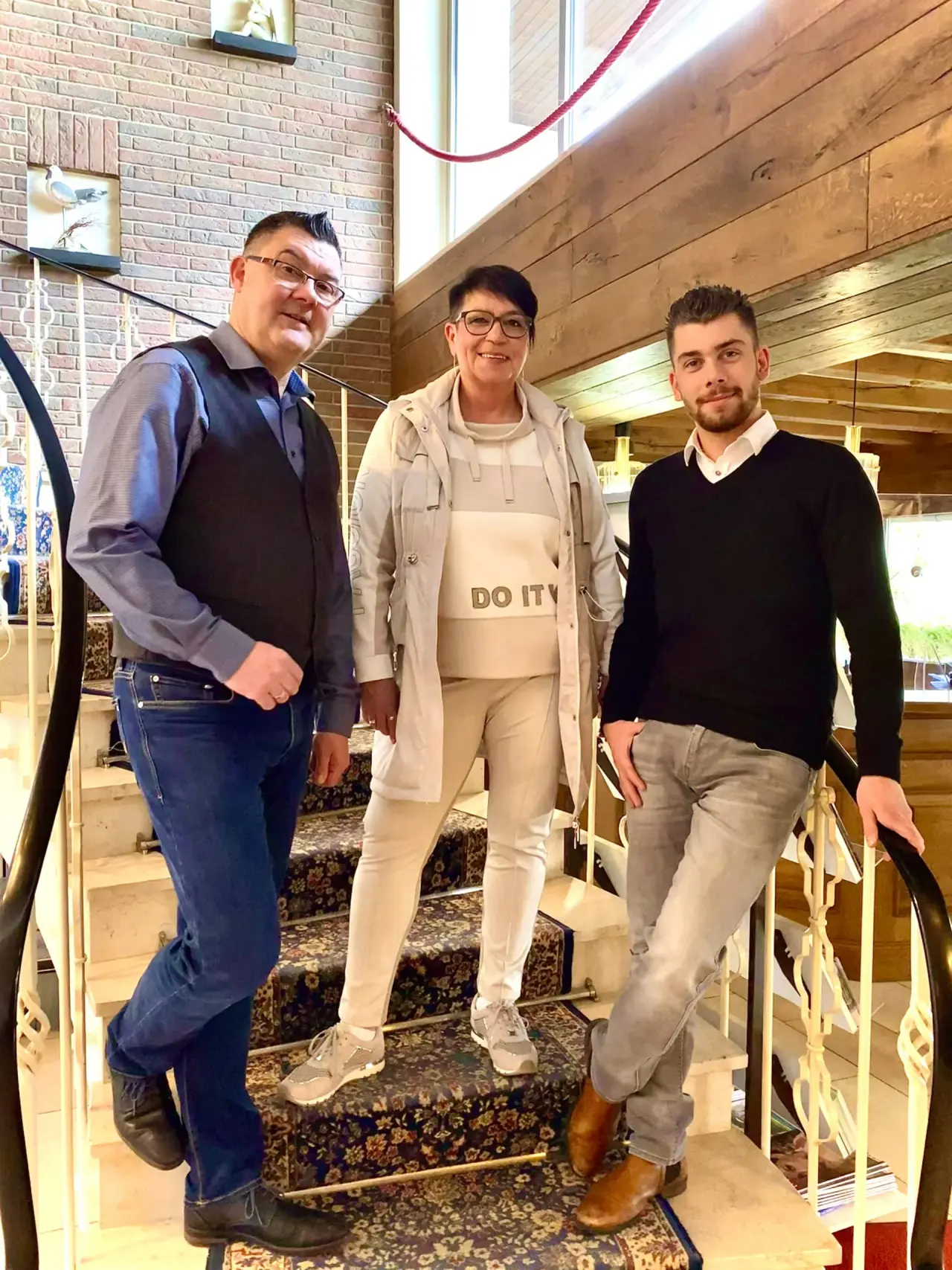 Drei lächelnde Personen auf einer geschwungenen Treppe im Innenbereich des Ferienhotel Stockhausen.