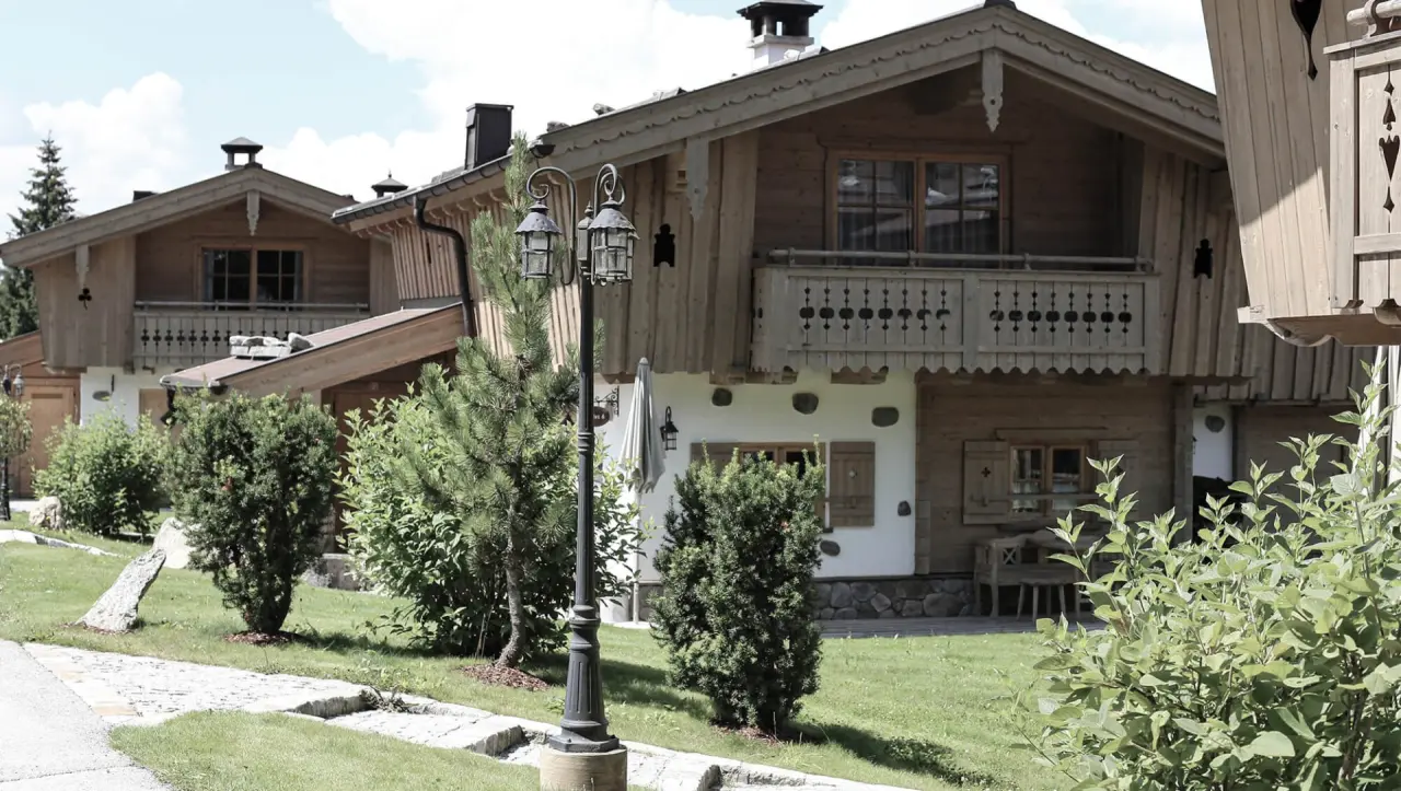 Traditionelle Holzchalets des INNs HOLZ Chaletdorf mit gepflegtem Garten und Laterne unter blauem Himmel.