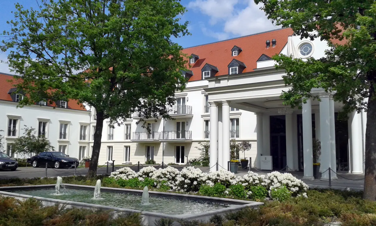 Eingangsbereich des Kempinski Hotel Frankfurt Gravenbruch mit Säulenportal, Springbrunnen und blühenden Büschen.