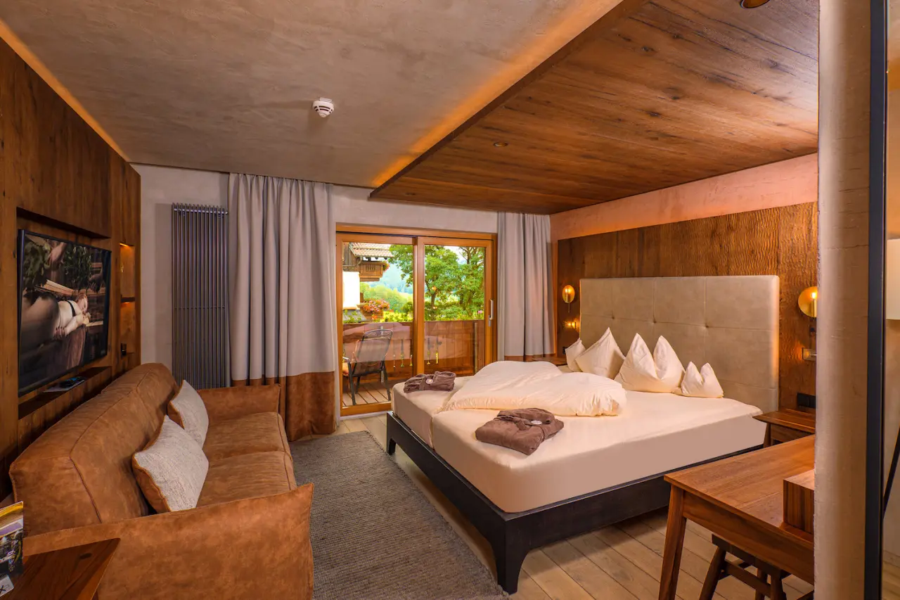 Gemütliches Hotelzimmer im Bayerwaldhof mit Doppelbett, Sofa und Balkonblick ins Grüne.
