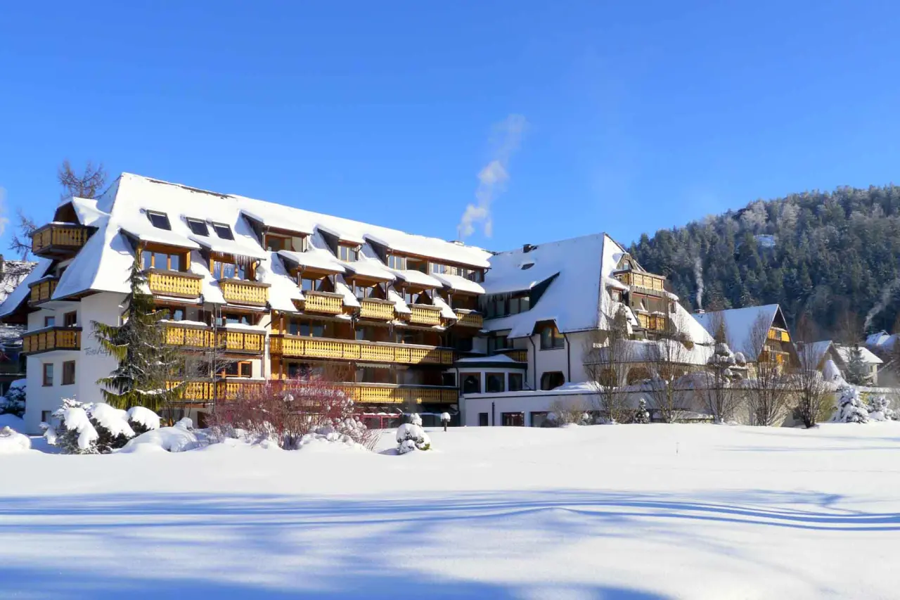 Winterliche Aussenansicht des Hotel Thomahof mit verschneiten Dächern und Balkonen vor einem blauen Himmel.