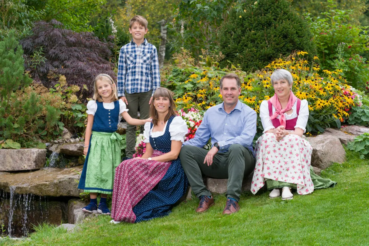 Familie in traditioneller Tracht im grünen Hotelgarten des Hotel Thomahof mit kleinem Wasserfall und Blumen.