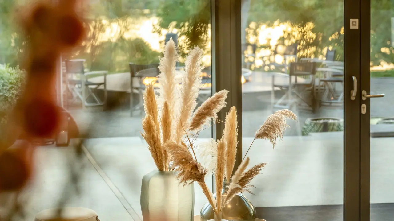 Dekorative Pampasgras-Vasen vor einem Fenster mit Blick auf die Terrasse des Seezeitlodge Hotels.