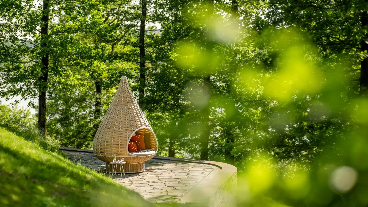 Gemütlicher Outdoor-Rattan-Sessel mit Kissen auf einer Steinterrasse im grünen Garten des Seezeitlodge Hotels.
