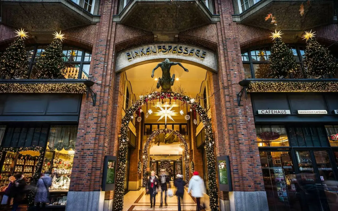 Festlich dekorierter Eingang der Einkaufspassage zum Park Hyatt Hamburg zur Weihnachtszeit mit Lichterketten und Tannenbäumen.