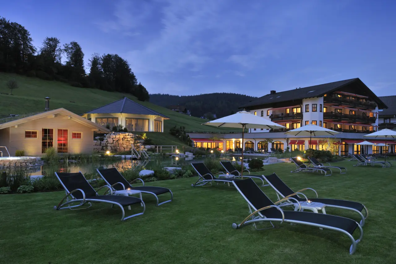 Abendliche Aussenansicht des Hotel Engel Obertal mit beleuchtetem Naturbadeteich, Sauna und Liegewiese im Schwarzwald.