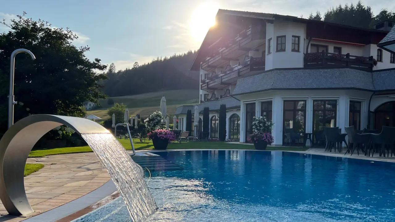 Aussenpool mit Wasserfall und Hotel Engel Obertal bei Sonnenuntergang. Idyllisches Wellness Resort im Schwarzwald.