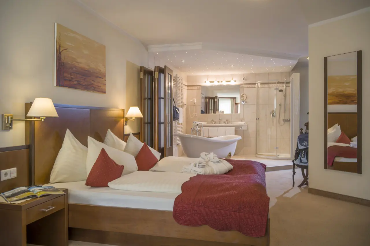 Komfortables Hotelzimmer im Alpin Family Resort Seetal mit Doppelbett, freistehender Badewanne und Dusche.