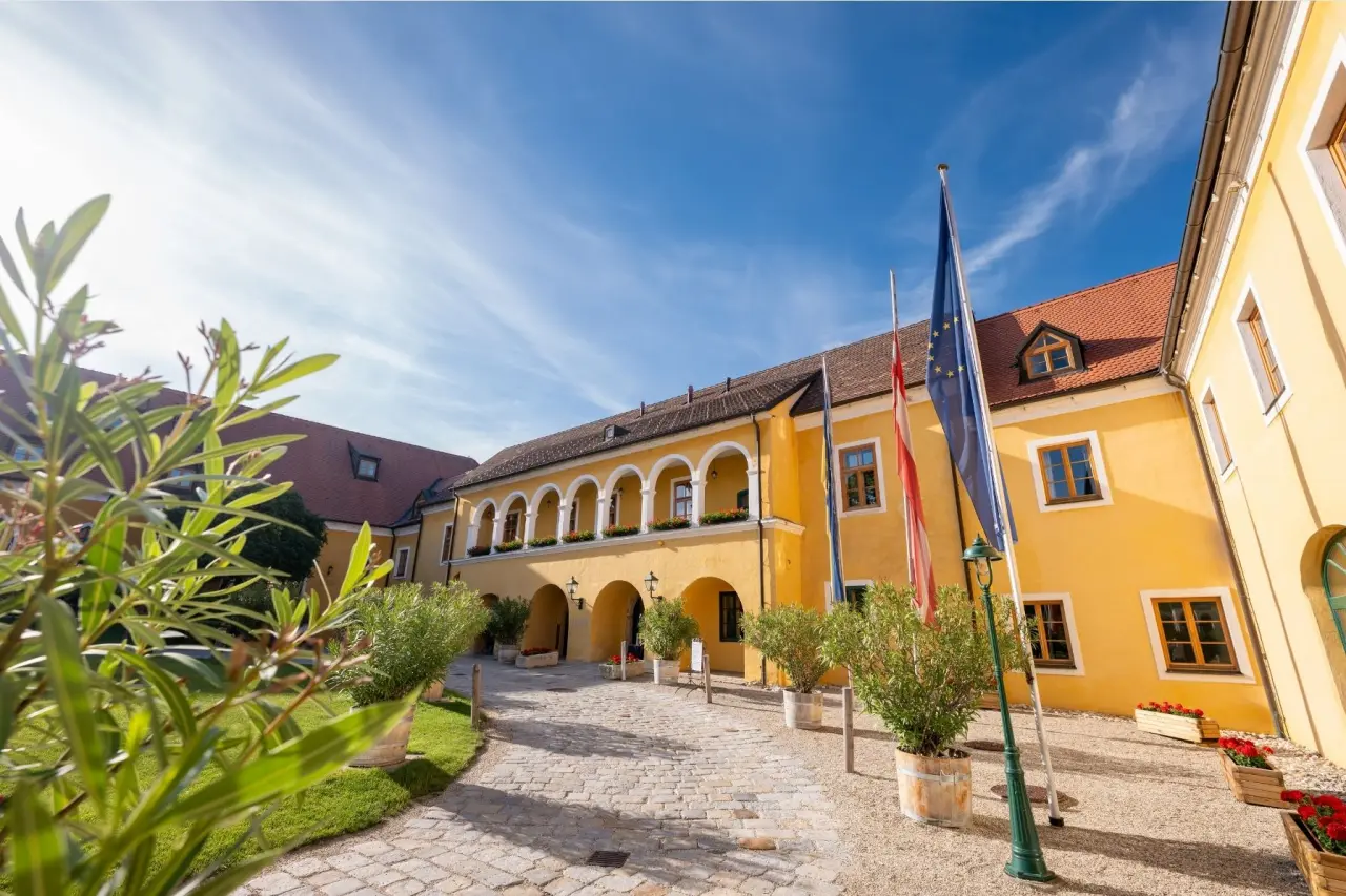 Aussenansicht des historischen Hotel Althof Retz mit gelber Fassade, Arkaden und gepflastertem Innenhof unter blauem Himmel.
