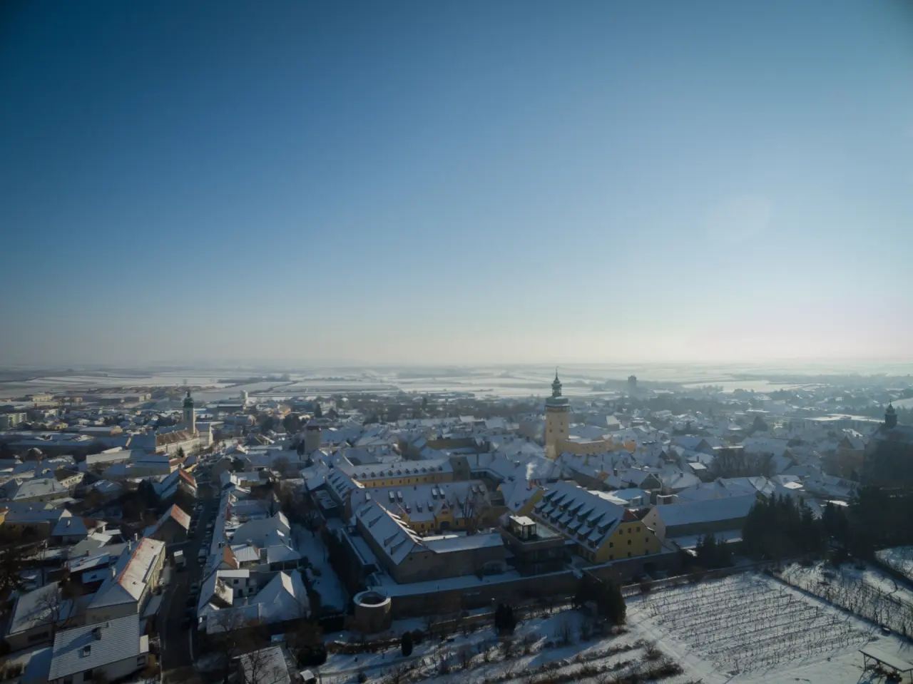 Luftaufnahme der verschneiten Stadt Retz mit dem Hotel Althof Retz und umliegenden Weinbergen im Winter.