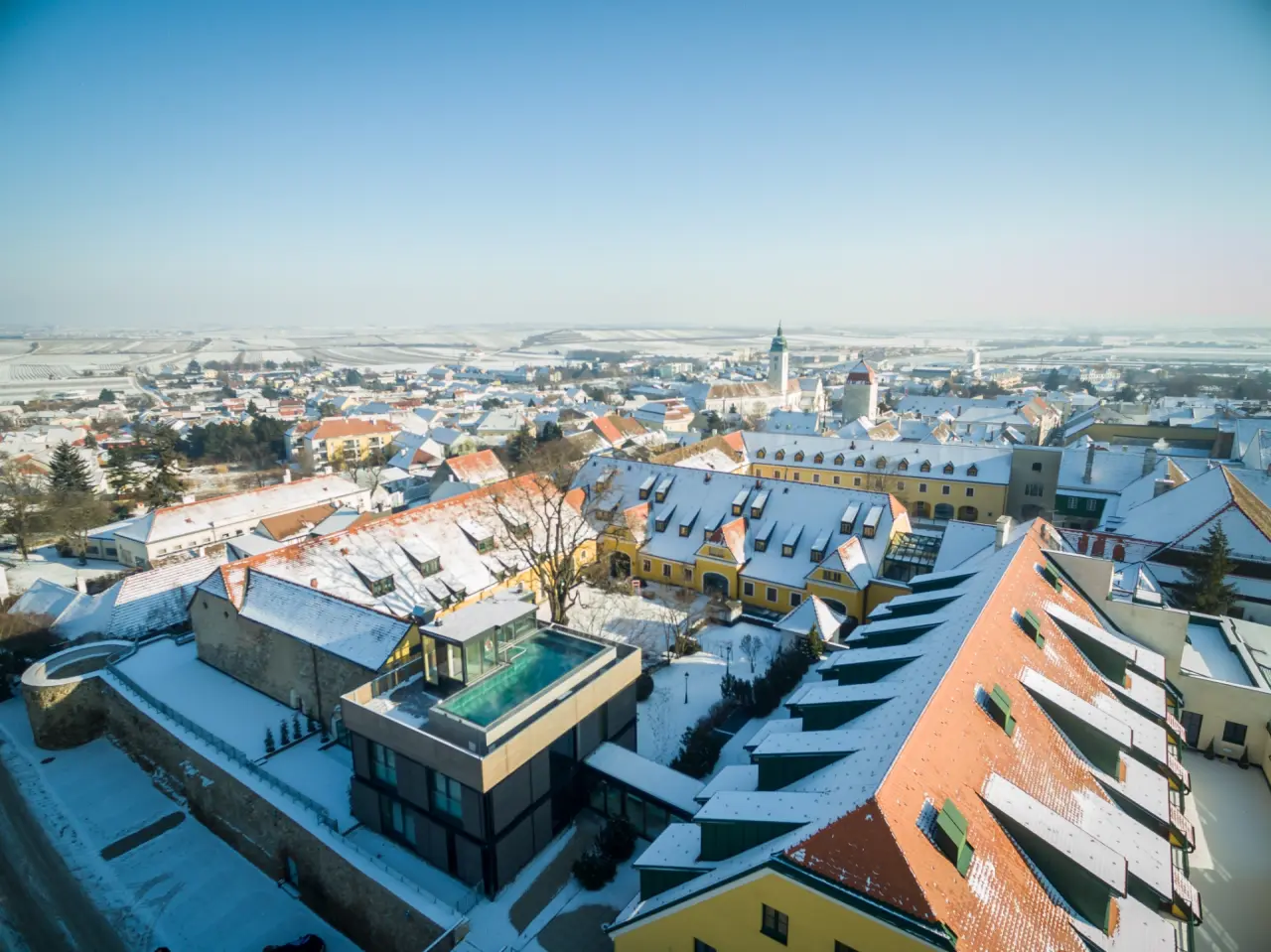 Luftaufnahme des Hotel Althof Retz im Winter mit verschneiten Dächern und einem beheizten Rooftop-Pool, umgeben von der historischen Stadt Retz und Weinbergen.