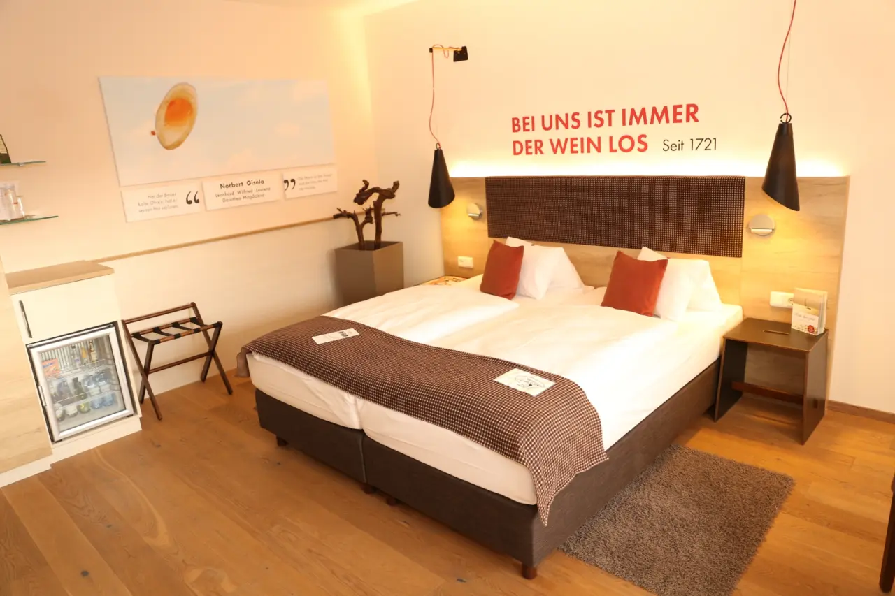 Gemütliches Doppelzimmer im Hotel Althof Retz mit Holzboden, bequemen Betten und Wanddekoration zum Thema Wein.