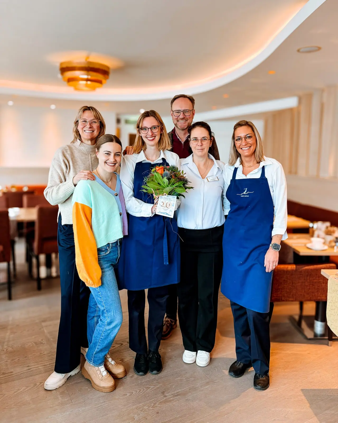 Freundliches Service-Team des Strandhotel Duhnen im Restaurant, eine Mitarbeiterin feiert Jubiläum mit Blumen.