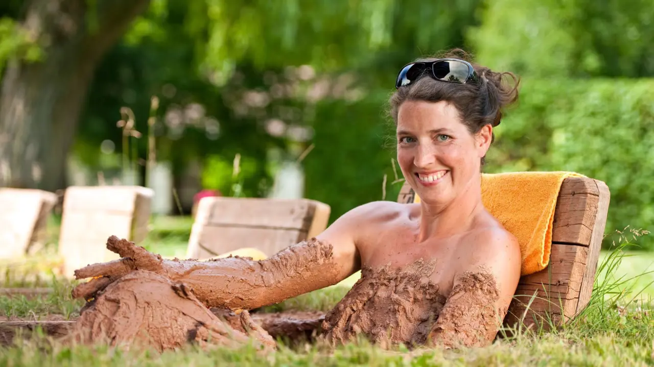 Lachende Frau genießt ein natürliches Moorbad im Grünen bei Menschels Vitalresort. Entspannung pur im Freien.