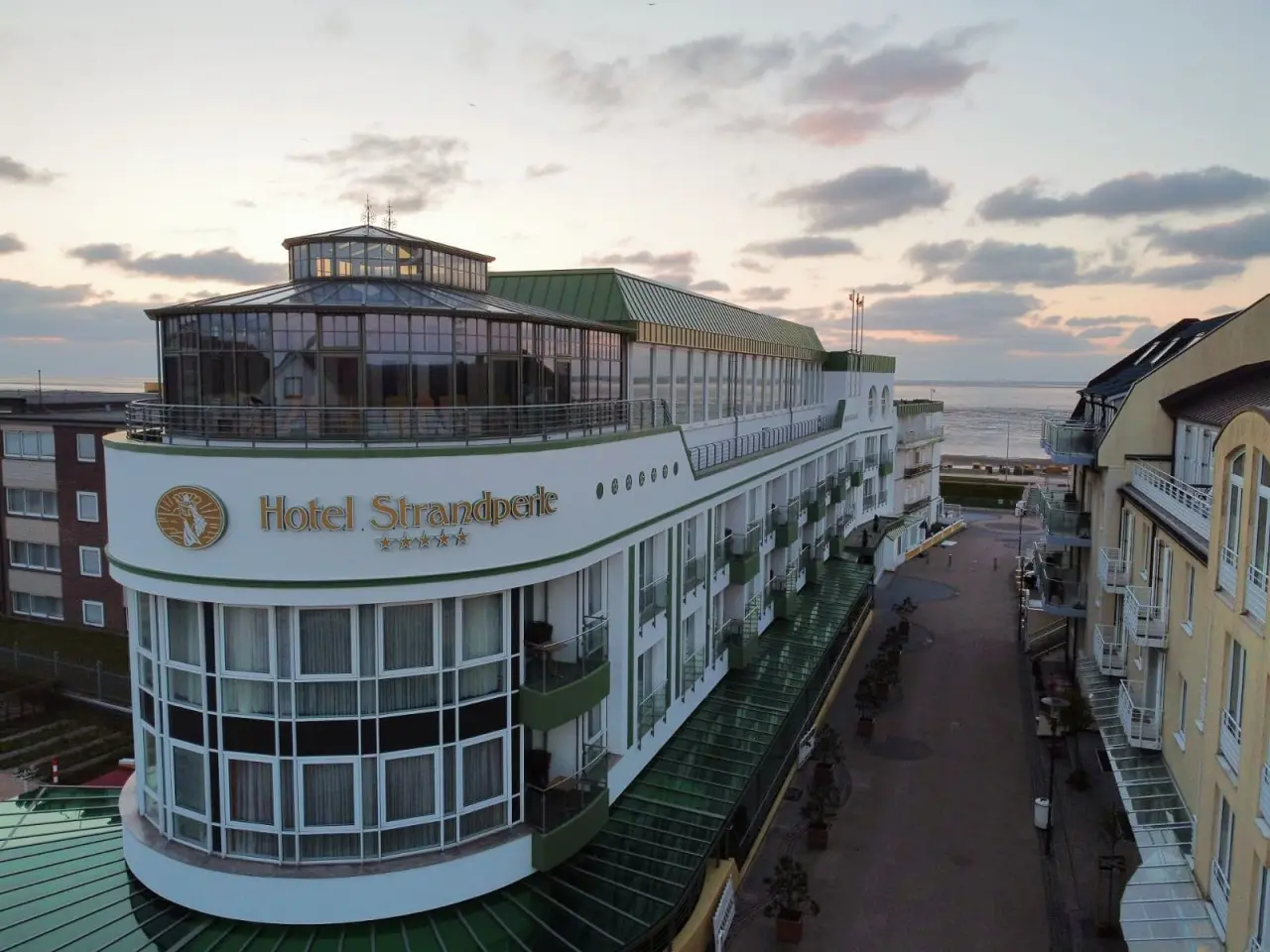 Aussenansicht des 4-Sterne Hotel Strandperle bei Sonnenuntergang mit Meerblick und Promenade.