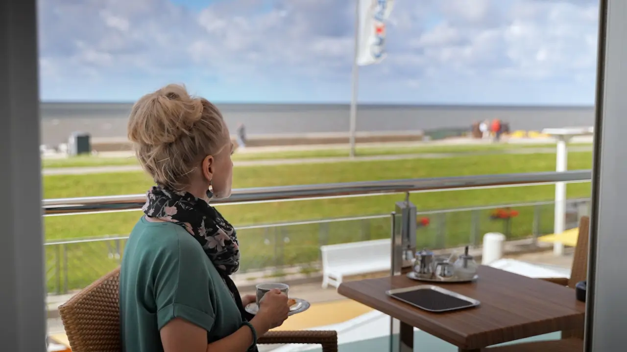 Frau genießt Kaffee auf der Terrasse mit Meerblick im Hotel Strandperle.