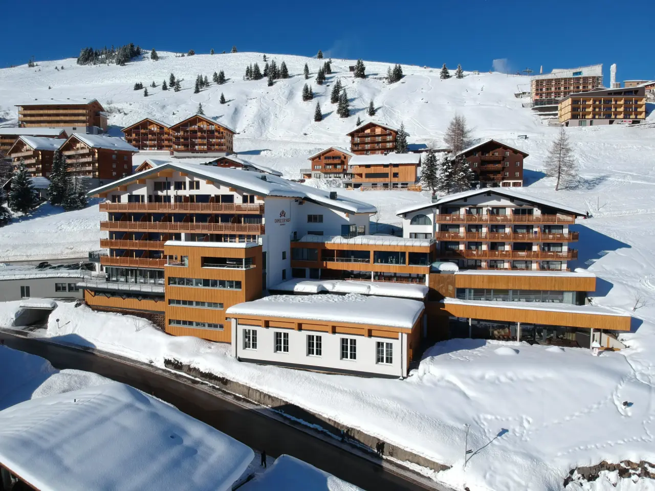 Panoramablick auf den Damülser Hof im Winter, umgeben von verschneiten Bergen und Skipisten.