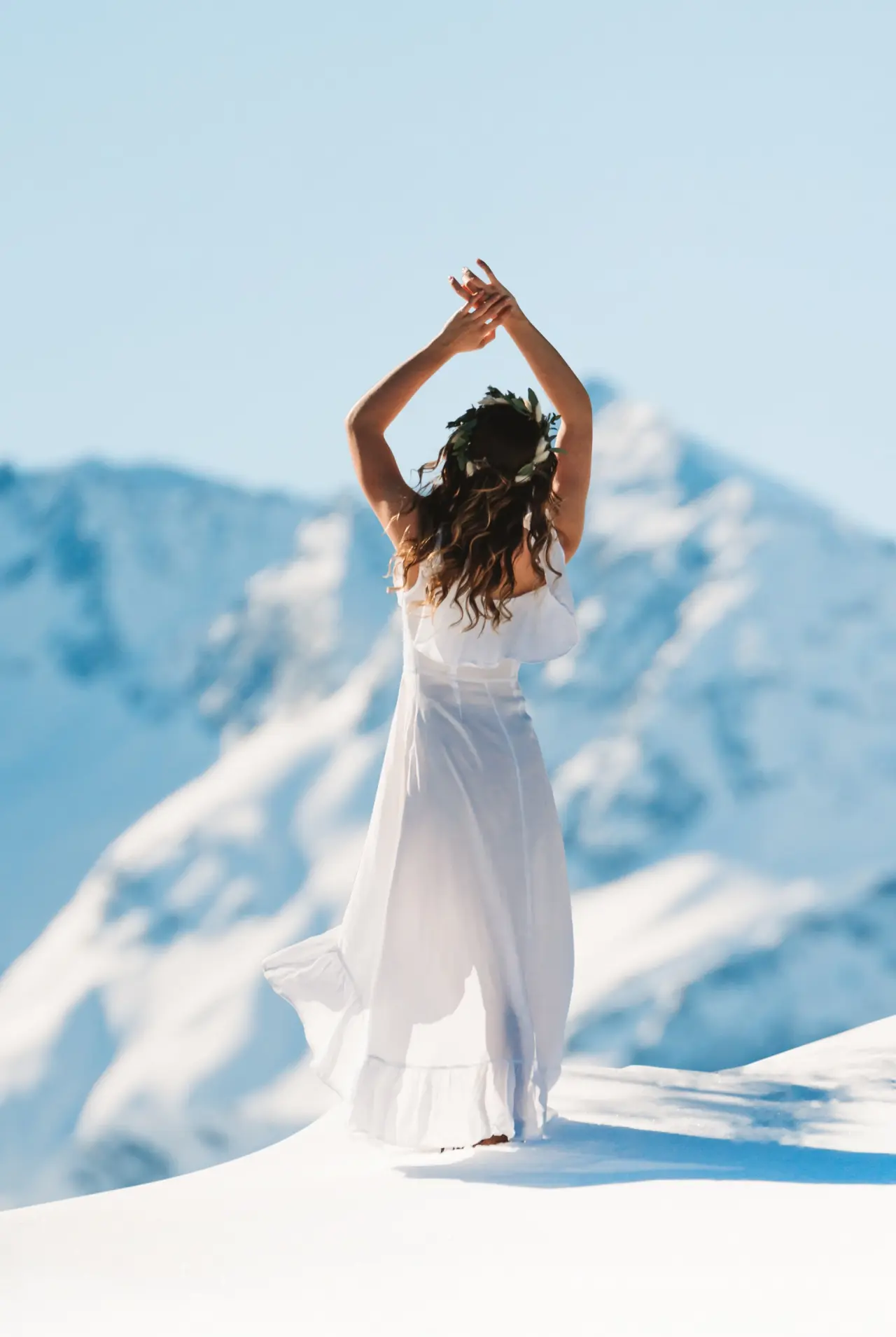 Frau im weissen Kleid mit Blumenkranz vor verschneiten Bergen, symbolisiert Freiheit und Natur im ZillergrundRock Resort.