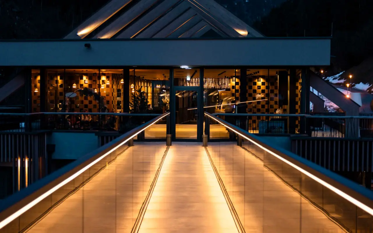 Modernes Eingangsgebäude des ZillergrundRock Luxury Mountain Resort bei Nacht mit beleuchtetem Steg und warmen Lichtern.