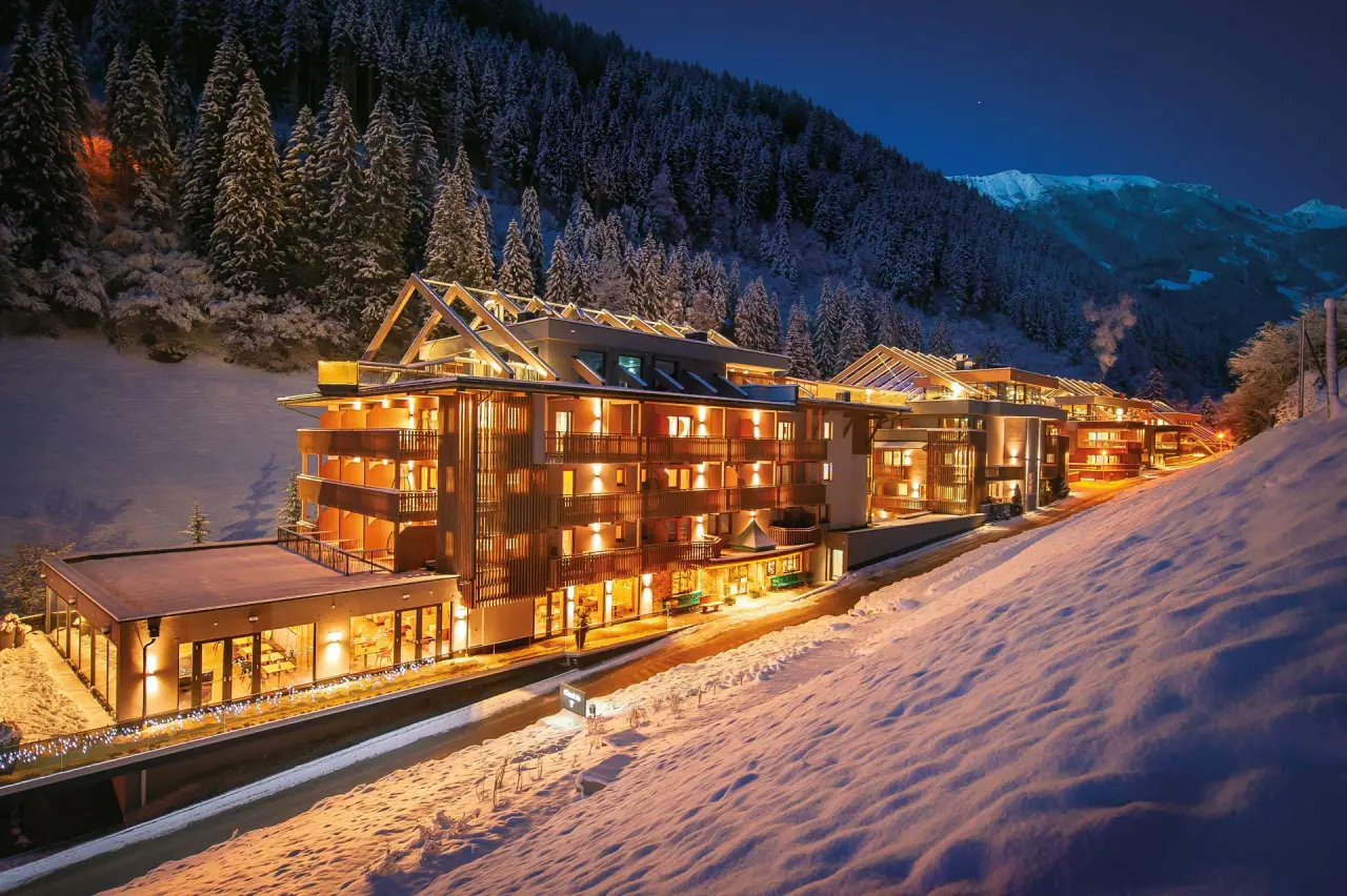 ZillergrundRock Luxury Mountain Resort bei Nacht im Winter. Beleuchtetes Hotel in verschneiter Alpenlandschaft mit Wald.