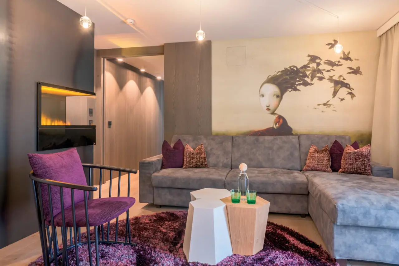 Gemütlicher Wohnbereich einer Suite im ZillergrundRock Luxury Mountain Resort mit Sofa, Sessel, Kamin und moderner Kunst.